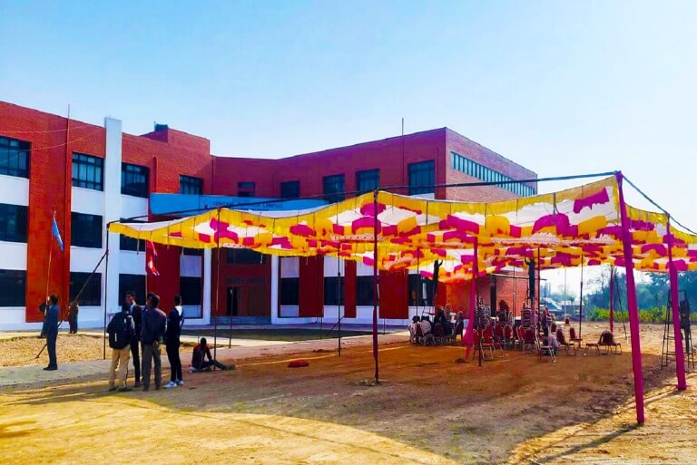 Outdoor event with colorful canopy at a red-brick building campus.