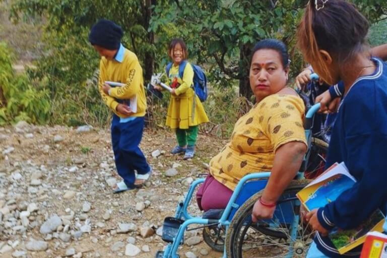 Woman in wheelchair with children on a rocky path.