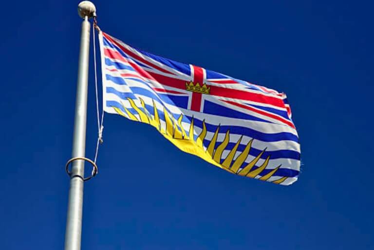 British Columbia flag waving under clear blue sky.