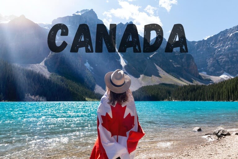 Woman in hat by Canadian lake with flag in scenic mountains.