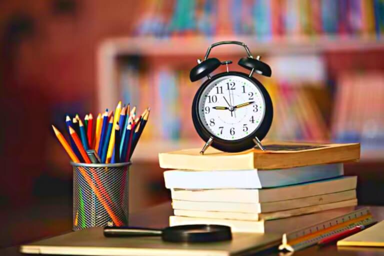 Vintage clock and colorful pencils on books in a study room.