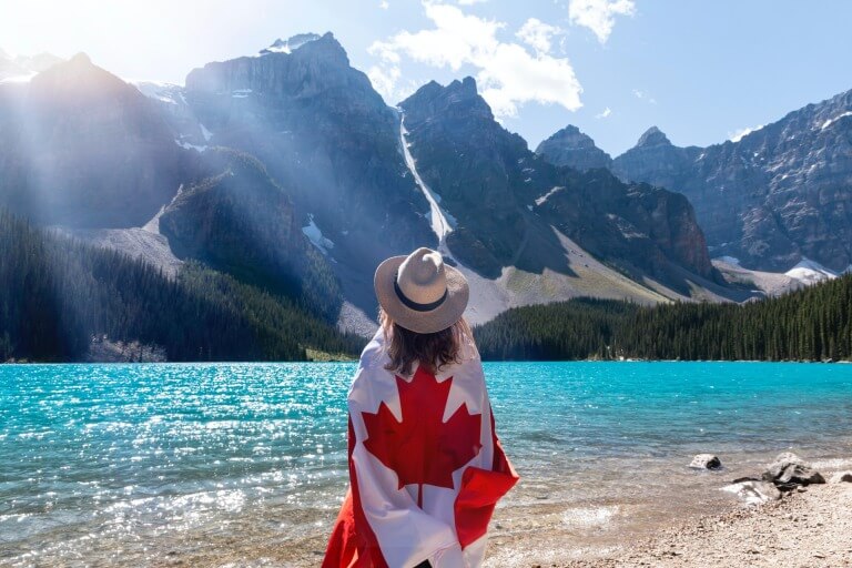 Person with Canadian flag at scenic mountain lake.