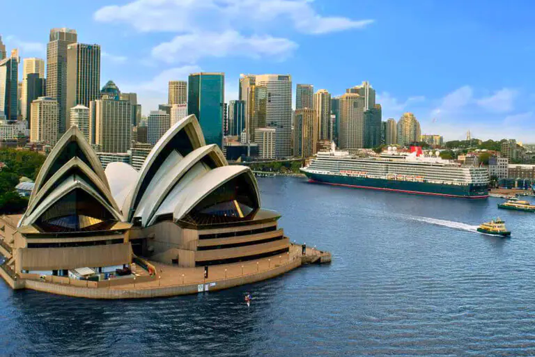 Sydney Opera House with skyline and cruise ship in harbor.