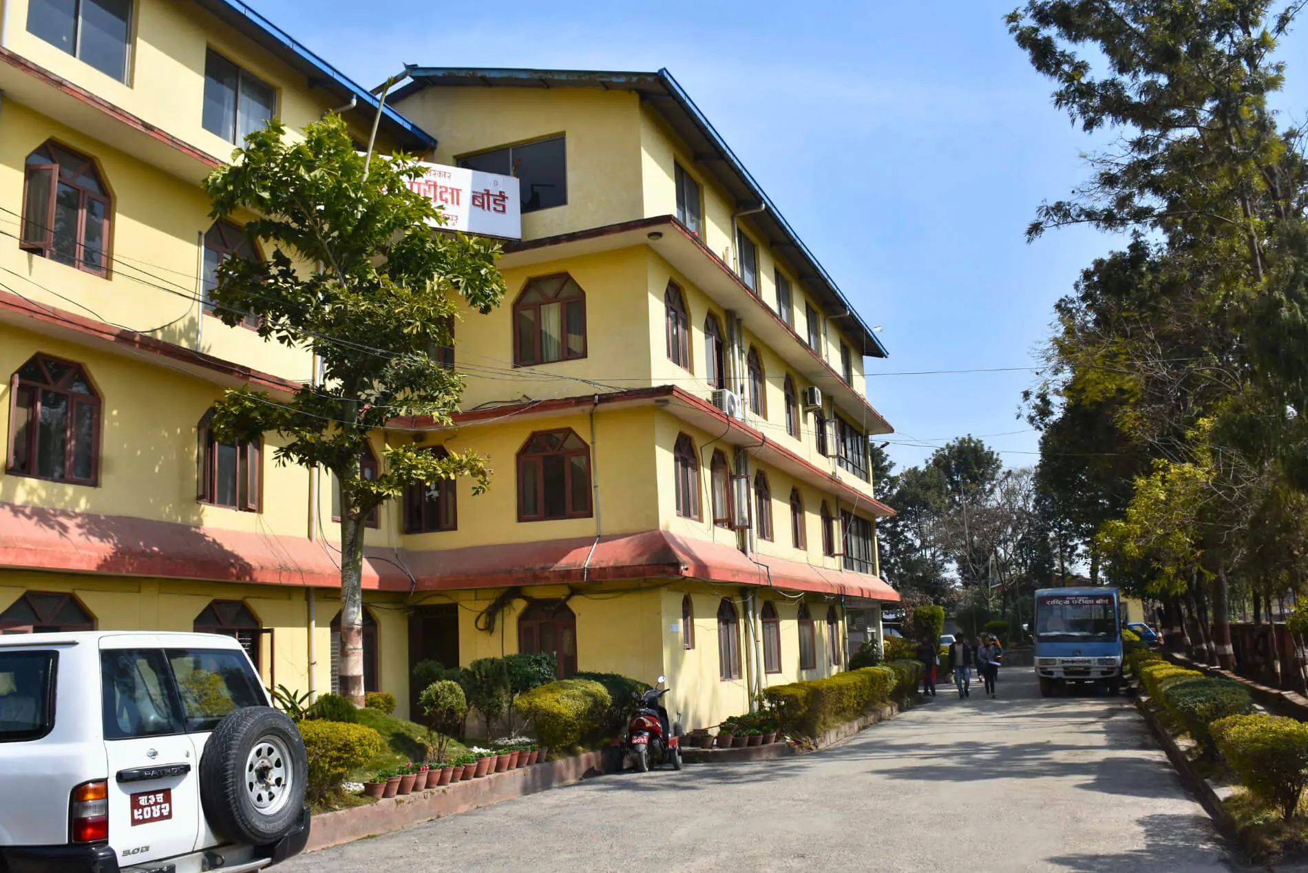 Yellow educational building with vehicles and greenery.