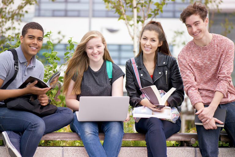 Group of students studying outdoors with books and laptop.