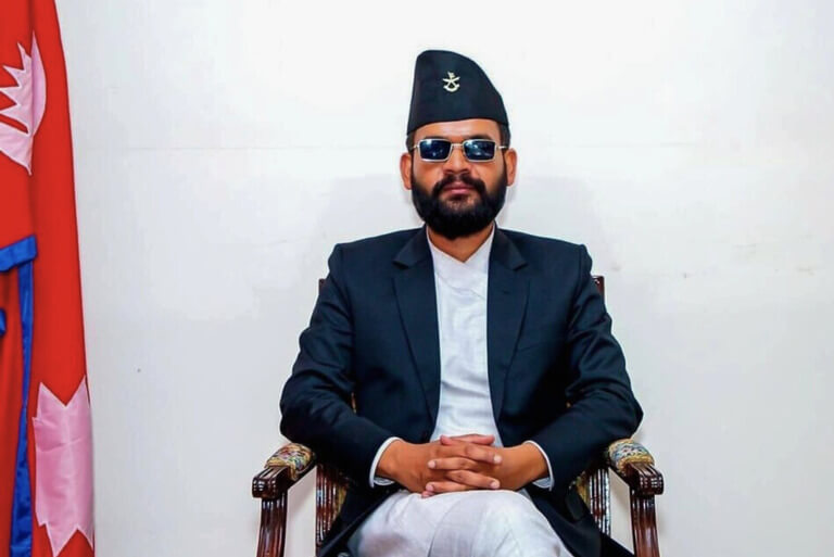 A man in traditional Nepali attire sitting with a flag.