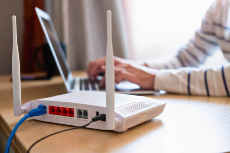 Wi-Fi router on desk with person using a laptop in background.