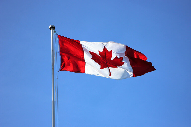 Canadian flag waving against a clear blue sky.