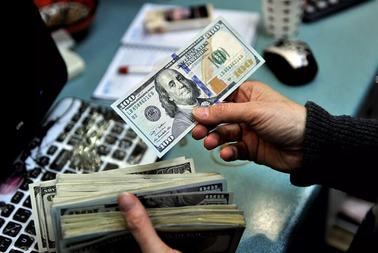 Person handling US dollar bills on a cluttered desk.
