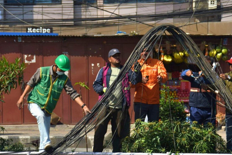 Workers handling overhead cables outdoors.
