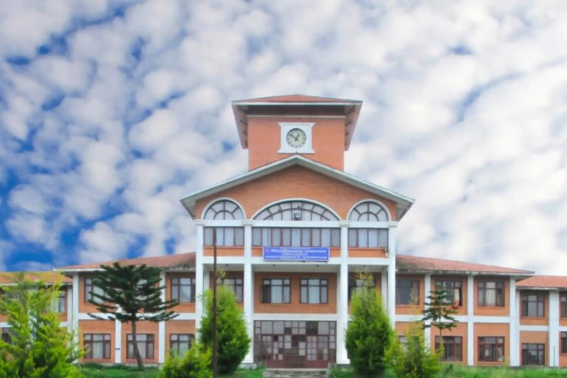 Tribhuvan University (1) Red brick clock tower building under cloudy sky.