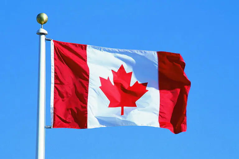 Canadian flag waving against a clear blue sky.