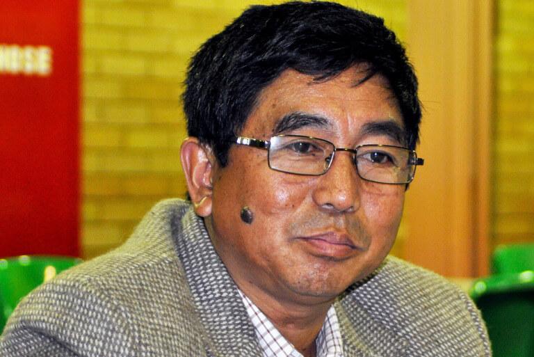 Man in glasses with a mole on his cheek indoors.