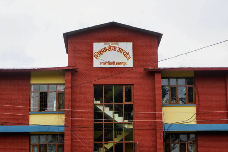 Red brick building with sign in Nepali text.