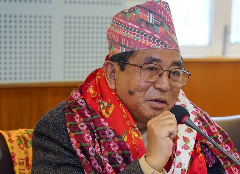 Man speaking into microphone wearing traditional Nepalese attire.