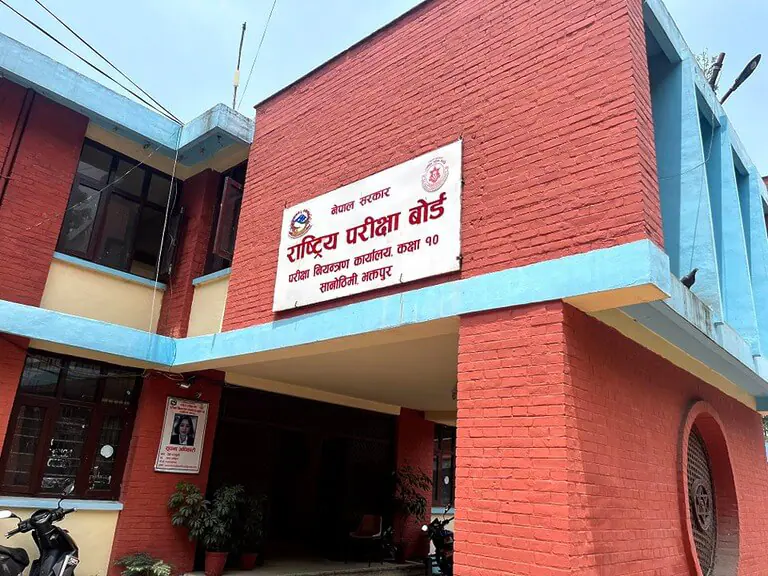 Red brick building with sign in Nepali language.