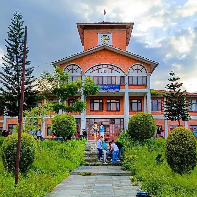 Red-brick building with clock tower and lush green landscaping.