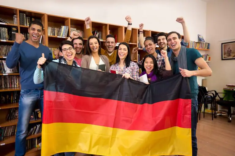 Group of cheerful people holding German flag in a library.