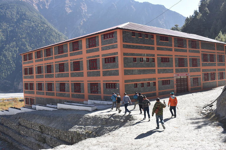 Orange and gray building with people walking nearby, mountainous background.