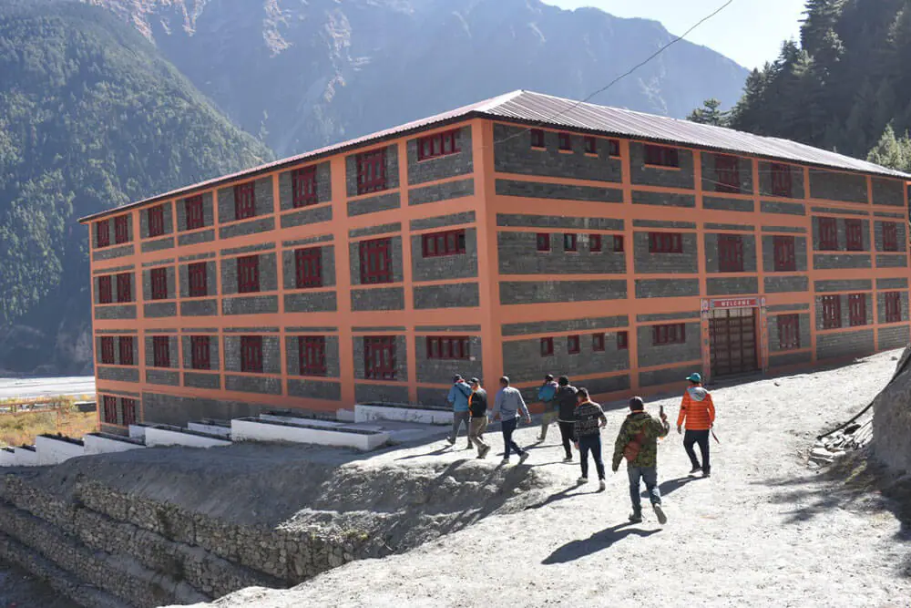 Orange and gray building with people walking nearby, mountainous background.