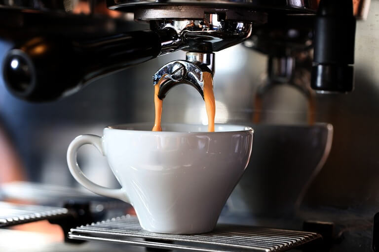 Espresso pouring into a white cup from coffee machine.