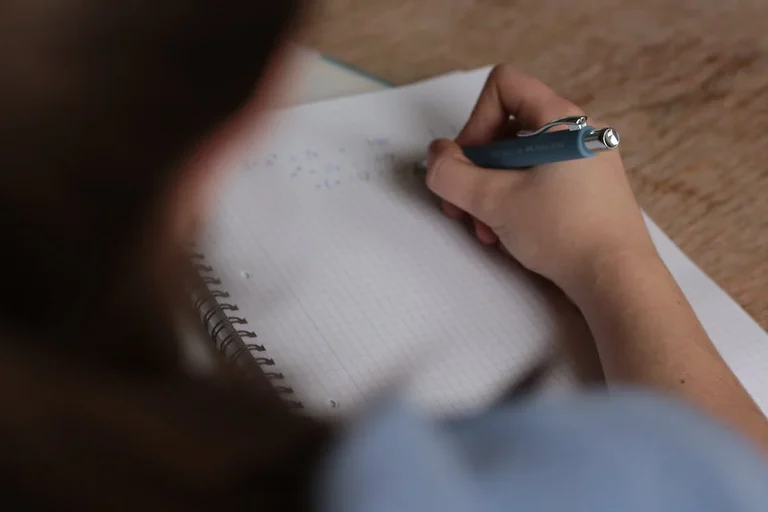 Person writing math equations in notebook.