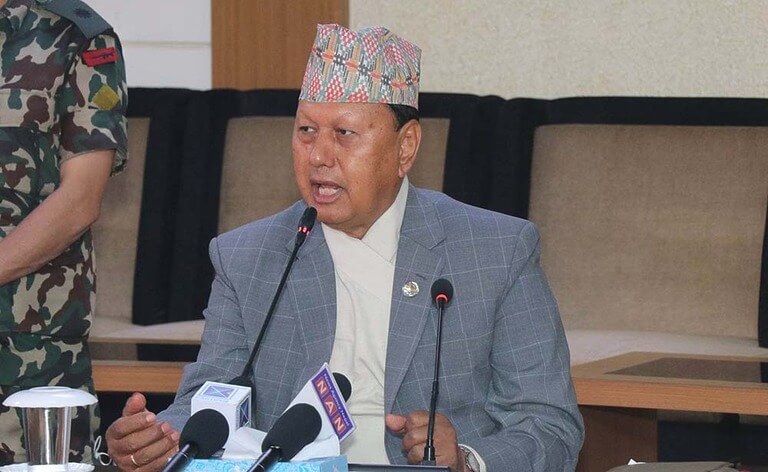 Man speaking at a press conference, wearing traditional Nepali cap.