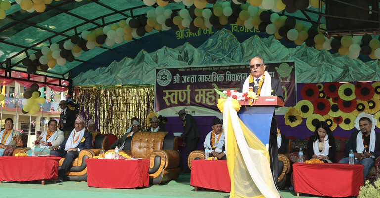 Outdoor event speech with seated attendees and mountain backdrop.
