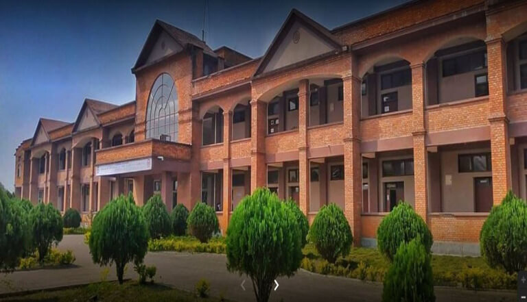 Red-brick building with lush greenery and cloudy sky.