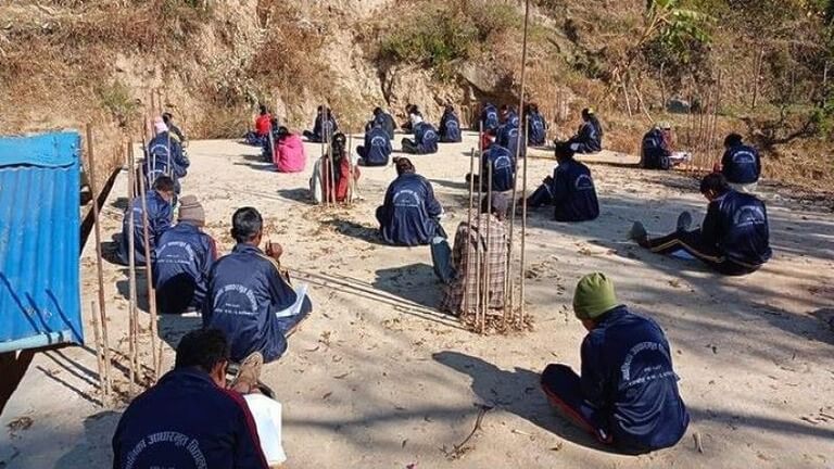 Outdoor classroom with students seated on the ground.