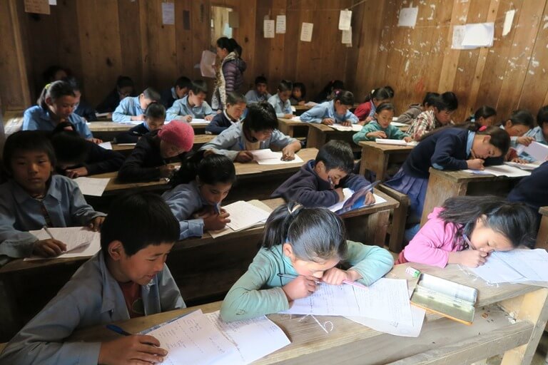 Children studying in a classroom with wooden desks.